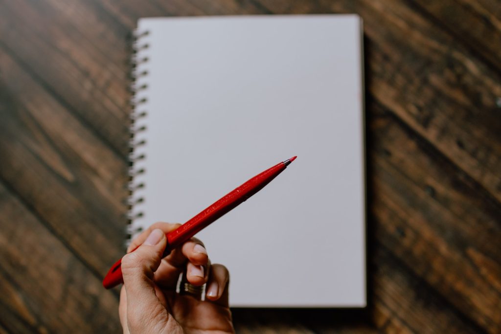 Person holds red pen in hand to indicate the tool often used in professional book editing.